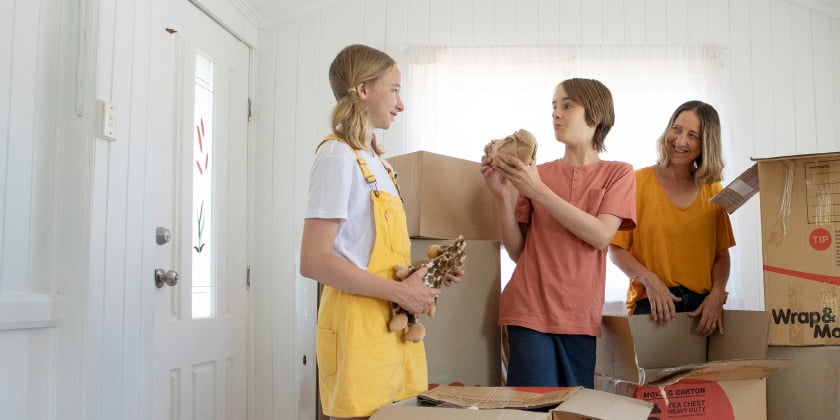 Three people unpacking boxes in a bright, white room with large windows.