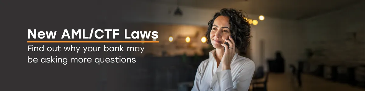 Banner displaying the text ‘New AML/CTF Laws - Find out why your bank may be asking more questions,’ alongside a person standing indoors whilst on the phone with warm lights in the background.