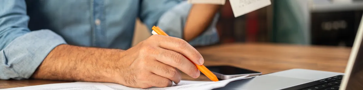 Person reviewing tax documents and a receipt while using a tablet and laptop, illustrating vigilance against ATO tax scams and protecting personal financial information.